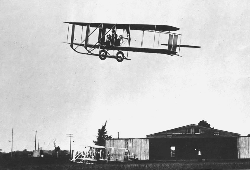 Un modello molto rudimentale di aeroplano vola ad alcuni metri dal suolo. Si tratta del Wright Flyer, brevettato il 23 marzo 1903.